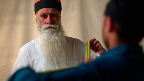 Fotografía-De-Estudio-De-Dos-Hombres-Sikh-Doblando-Tela-Para-Un-Turbante-Contra-Un-Fondo-Liso-En-Tiempo-Real